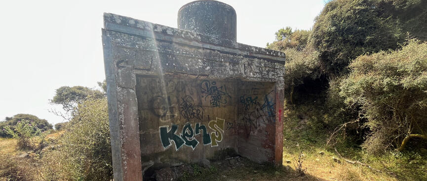 A square concrete structure is tagged with graffiti and open on one side.