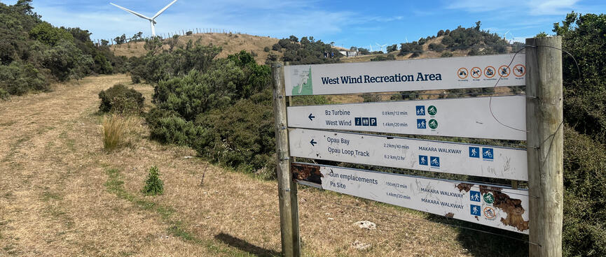 A slatted sign board lists nearby trails in the West Wind Recreation Area. Crossed out icons prohibit camping, dogs, motorbikes, fires and guns.