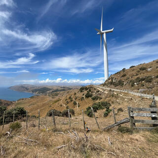 A wind turbine sits on top of a hill, which offers views of the sea and coastline.