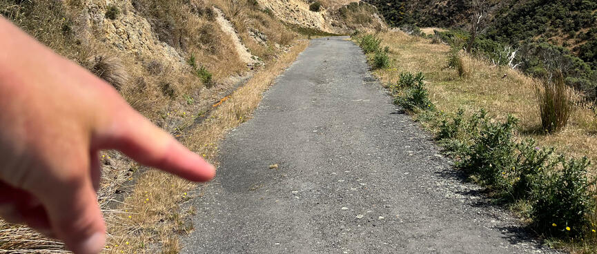 A hand points down a steep concrete road.