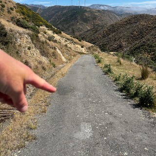 A hand points down a steep concrete road.