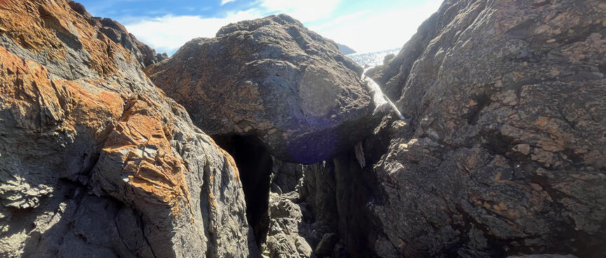 A large boulder is wedged into the gap between two slabs of rock, blocking the way.