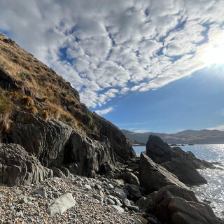 The gap between a steep tussock-clad hill and angled rocks rising from the sea.
