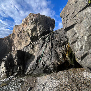 Two ropes hang down the face of a wide sloping rock, which juts into the sea.