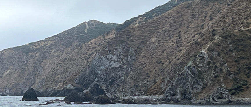 A section of coastline shows two rock ribs which block the beach, with steep hillsides around them.