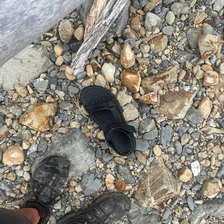 A black sandal lies face down on the rocky beach.