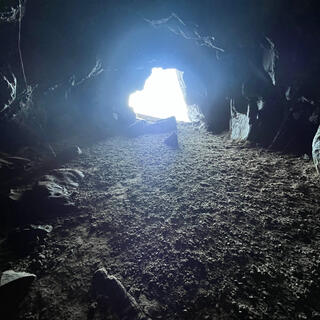 A cave with a low ceiling is illuminated by a hole in the far wall.