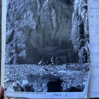 Three men sit outside the cave, John Magurk at left. Someone has written ʼ1960s?ʼ.