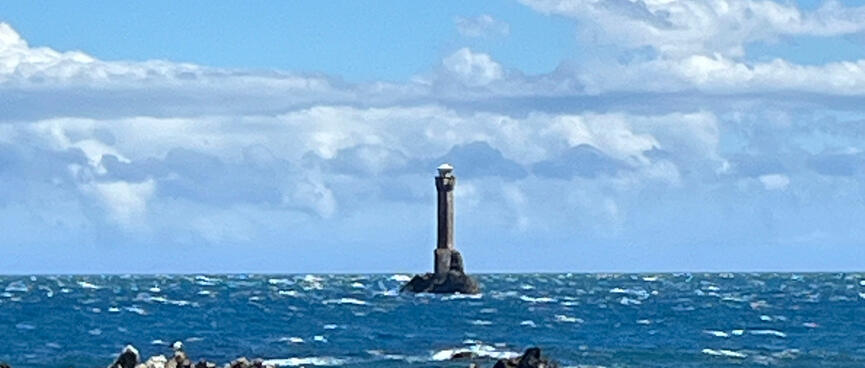 A tall structure in stormy sea beyond the rocky coastline.