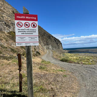 A ʼHealth Warningʼ sign on the side of a coastal trail.