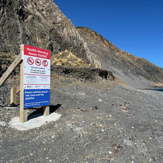 A ʼHealth Warning Sewer Outfallʼ sign on the side of a coastal trail.