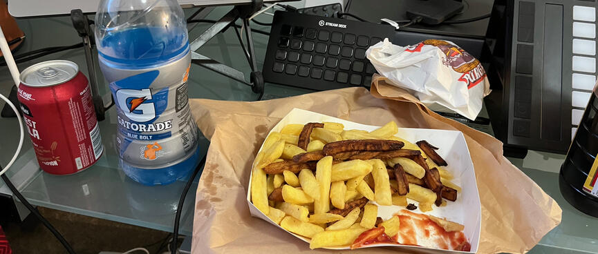 A cardboard tray containing gold and brown fries, a bottle of blue Gatorade and a can of cola.