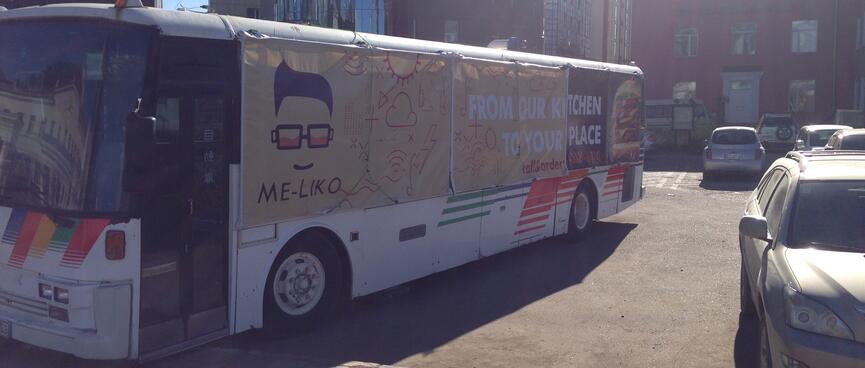 Advertising for the Me-liko food catering service is draped over the windows of a bus.