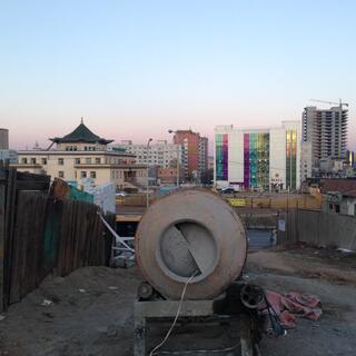 A concrete mixer stands on an empty section. In the distance the skyline is a mixture of traditional temples and garish high rises.