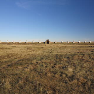 A long wall on the far side of a grassy field.