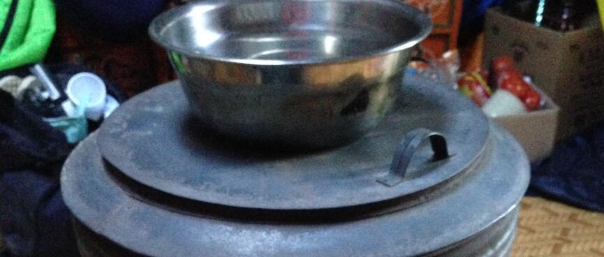 A bowl of water sits on top of a round stove containing a fire.