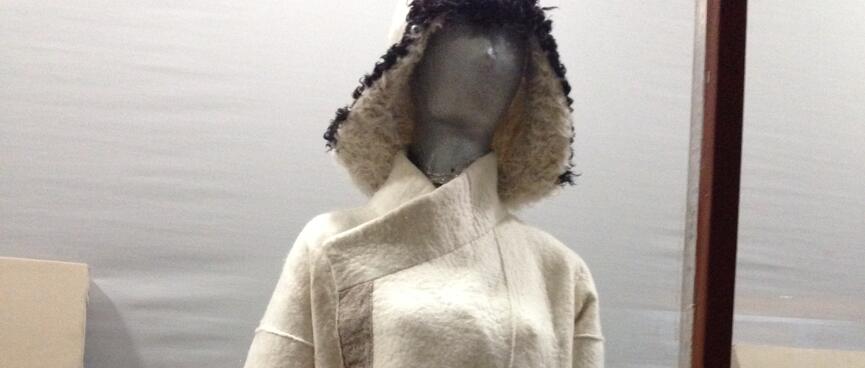 A mannequin wears a furry hat and a white cloak with light brown belt and trim.