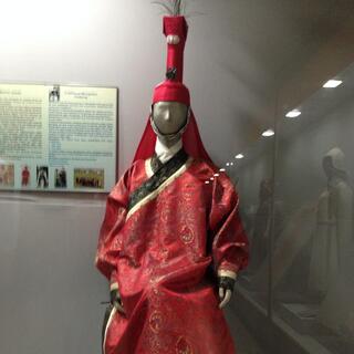 A mannequin wears a ceremonial cloak and a matching hat with a tall narrow extension.