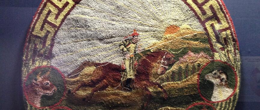 A felt badge showing a rider on a galloping brown horse, under a bright sun. Four other animals are featured on the border of the badge.