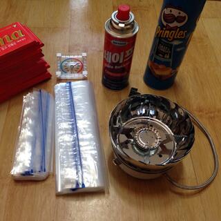 A fold up gas burner and cartridge, chocolate, chips and plastic bags.