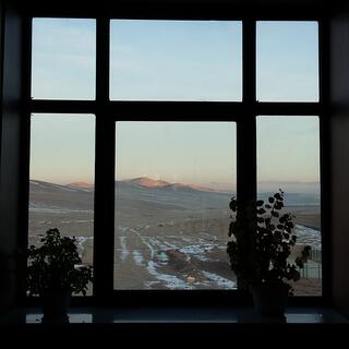 Six window panes frame a view of snowy ground, distant mist and sun kissed mountains.