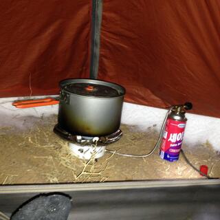 A camping pot sits on a gas cooker in the corner of my tent. The gap between the tent and the ground is packed with snow.
