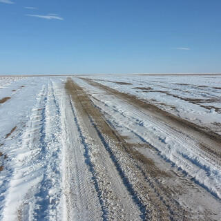 Wide brown tyre tracks cut a path through a snowy field.