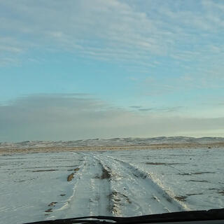 View out the windscreen to tyre tracks through the snow, intermittently revealling patches of brown sand.