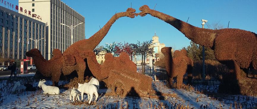 Statues of brown dinosaurs and white sheep and goats.