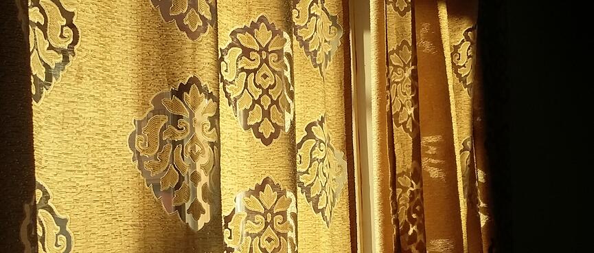 Sunlight illuminates golden curtains adorned with ornate diamond motifs.
