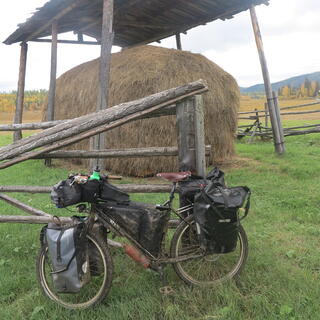 My mud-caked bike is dwarfed by a mound of grass, protected by an open-sided shed.