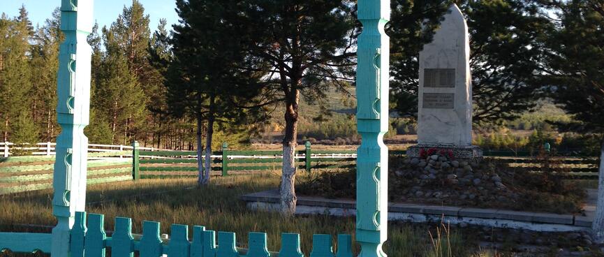 A small stone memorial sits behind an elaborate teal wooden gate.
