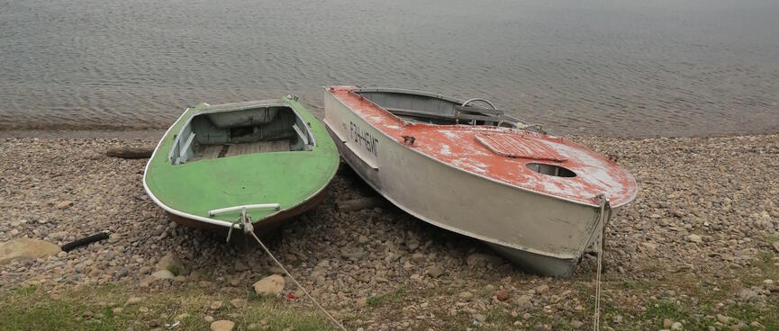 Red and green boats on the beach, tied up side by side.