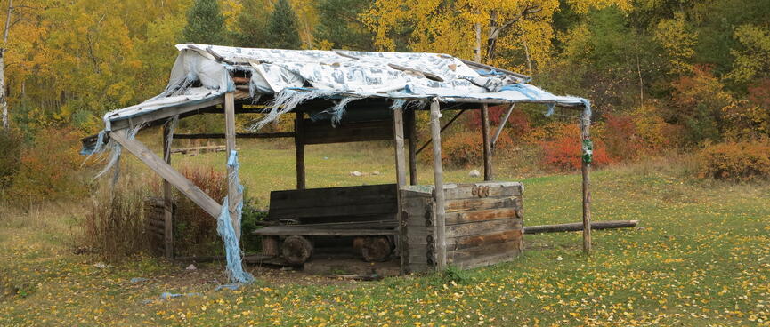 A wooden bench under a frayed plastic roof.