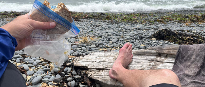 Resting my bare feet on beach pebbles and driftwood while eating a peanut butter sandwich.