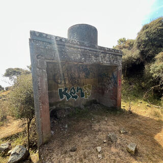 A square concrete structure is tagged with graffiti and open on one side.