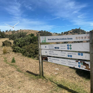 A slatted sign board lists nearby trails in the West Wind Recreation Area. Crossed out icons prohibit camping, dogs, motorbikes, fires and guns.