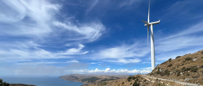 A wind turbine sits on top of a hill, which offers views of the sea and coastline.