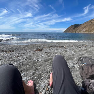 Sitting on the beach with wet shorts, my bare feet are covered in small pebbles.