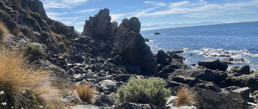 A rocky outcrops almost blocks the beach ahead, but thereʼs a narrow pass between the hillside and the rocks.