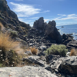 A rocky outcrops almost blocks the beach ahead, but thereʼs a narrow pass between the hillside and the rocks.