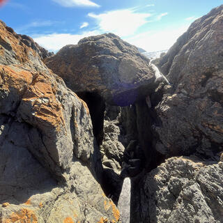 A large boulder is wedged into the gap between two slabs of rock, blocking the way.