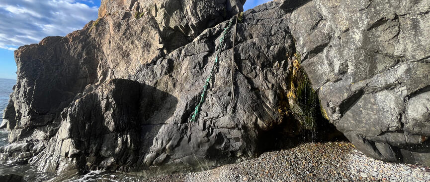 Two ropes hang down the face of a wide sloping rock, which juts into the sea.