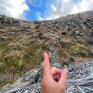 A finger points at the very steep grass and rock bank heading to the top of the hill.