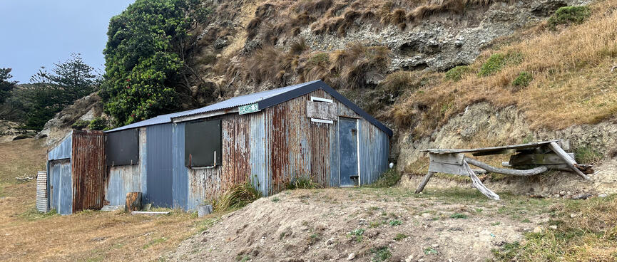 A rusting metal house with metal shutters over the windows, and a DIY picnic table.