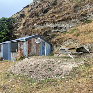 A rusting metal house with metal shutters over the windows, and a DIY picnic table.