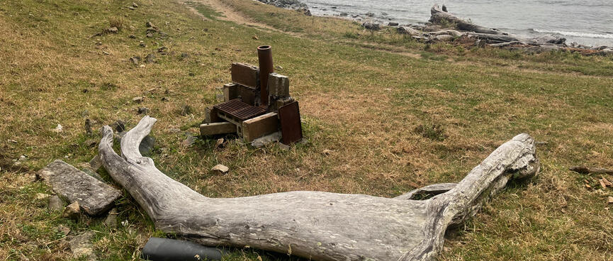 A curved piece of driftwood provides seating around a DIY stove.