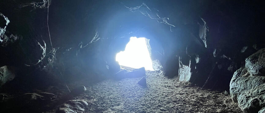 A cave with a low ceiling is illuminated by a hole in the far wall.
