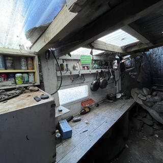 A long wooden bench, shelves covered in beer cans, a cooking area with a chimney and a wooden cabinet.