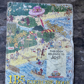 The cover of a 1B5 exercise book features a whacky illustration of a UFO attacking a beach scene.